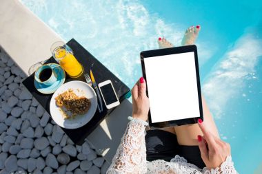 Yüzme havuzunda otururken dijital tablet kullanan kadın