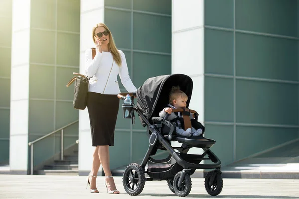 Donna d'affari che parla al telefono e spinge passeggino bambino — Foto Stock