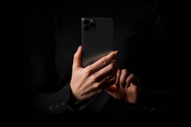Elde cep telefonu olan ve ekrana parmağıyla dokunan kişi, siyah arkaplanda izole edilmiş bir fotoğraf.