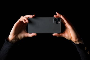 El ele tutuşan ve cep telefonuyla fotoğraf çeken biri, siyah arka planda izole edilmiş bir fotoğraf.