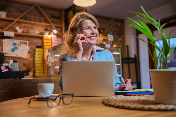 Woman in cafe talking on phone and working with laptop