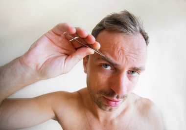 Adam cımbızla kaşlarını yoluyor.