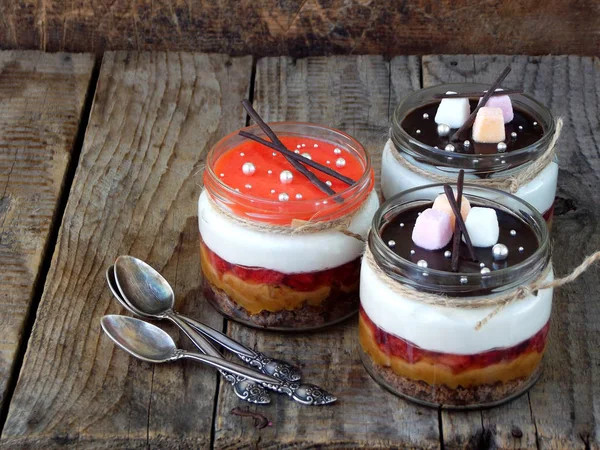 Επιδόρπιο cheesecake σε γυάλινο βάζο σε ξύλινο υπόβαθρο.: σοκολάτα, μπισκότο, αλατισμένα καραμέλα μαρμελάδα φράουλα, τυρί μους, σοκολάτα καθρέφτη λούστρο. Επιλεκτική εστίαση. Χώρο αντίγραφο — Φωτογραφία Αρχείου