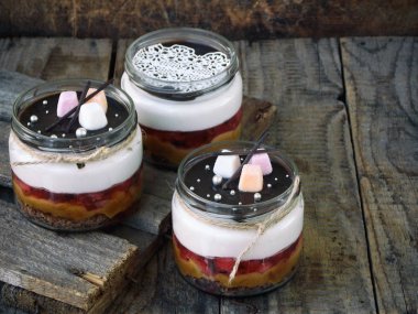 Cheesecake tatlı cam üzerinde ahşap arka plan.: Çikolata Bisküvi, tuzlu karamel, çikolata ayna sır çilekli jöle, peynir mus. Seçici odak. Kopya alanı