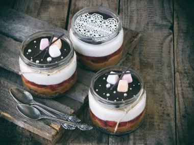 Cheesecake tatlı cam üzerinde ahşap arka plan.: Çikolata Bisküvi, tuzlu karamel, çikolata ayna sır çilekli jöle, peynir mus. Seçici odak. Kopya alanı