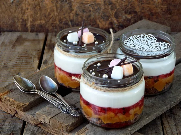 Sobremesa de bolo de queijo em jarra de vidro em fundo de madeira. : biscoito de chocolate, caramelo salgado, geleia de morango, mousse de queijo, esmalte de espelho de chocolate. Foco seletivo. Espaço de cópia — Fotografia de Stock