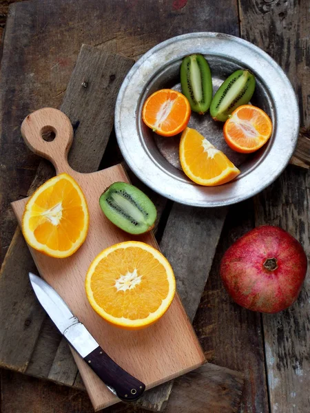 Композиция срезанных фруктов, апельсина, киви, мандарина, граната на деревянной доске и тарелке. Селективный фокус — стоковое фото