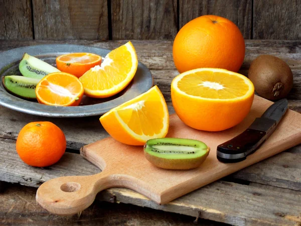 Composition du fruit coupé, orange, kiwi, mandarine, grenade sur une planche de bois et une assiette. Concentration sélective — Photo