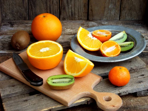 Composition of the cut fruit, orange, kiwi, tangerine, pomegranate on a wooden board and a plate. Selective focus — Stock Photo, Image