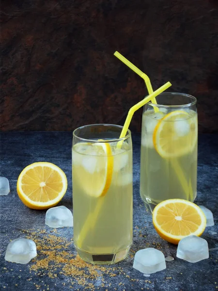 Twee glazen van koude zelfgemaakte limonade met citroen segmenten, ijsblokjes, bruine suiker en rietjes op donkere achtergrond. Kopiëren van ruimte — Stockfoto