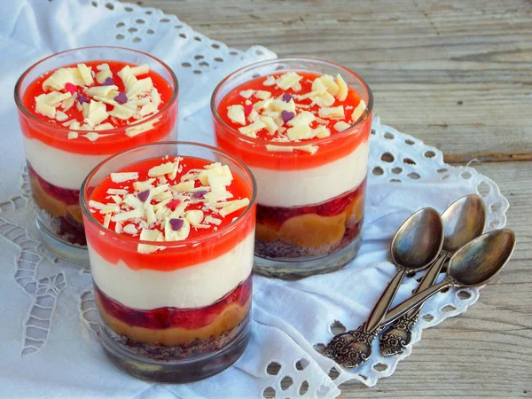Cheesecake dessert in glass jar on wooden background.: chocolate biscuit, salted caramel, strawberry jelly, cheese mousse, chocolate mirror glaze. Selective focus. Copy space — Stock Photo, Image
