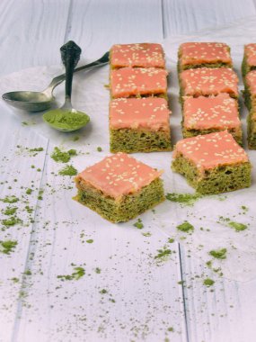 Japon çay matcha ile yeşil kek hafif ahşap zemin üzerine çikolata pembe kumlama kaplı. Seçici odak. Kopya alanı