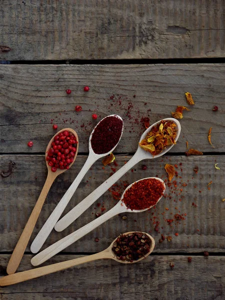 Red spices on a wooden background. Pink pepper, sumac, paprika, marigold, Sichuan pepper.