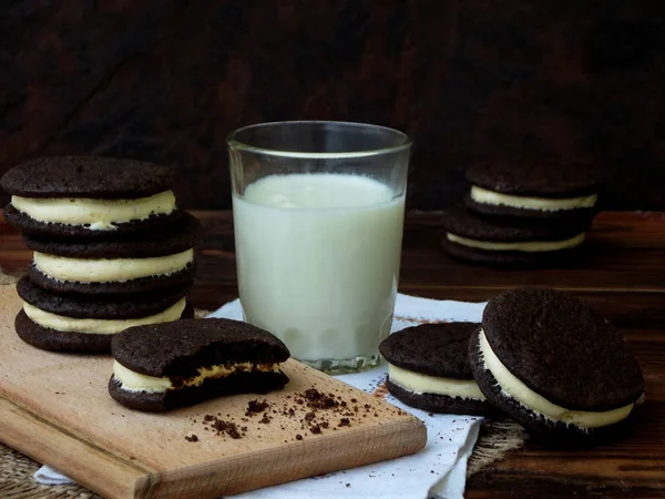 Hausgemachte Schokoladenkekse mit weißer Marshmallow-Sahne und einem Glas Milch auf dunklem Hintergrund. Selektiver Fokus. — Stockfoto