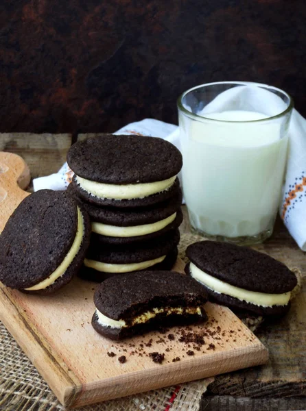 Hausgemachte Schokoladenkekse mit weißer Marshmallow-Sahne und einem Glas Milch auf dunklem Hintergrund. Selektiver Fokus. — Stockfoto