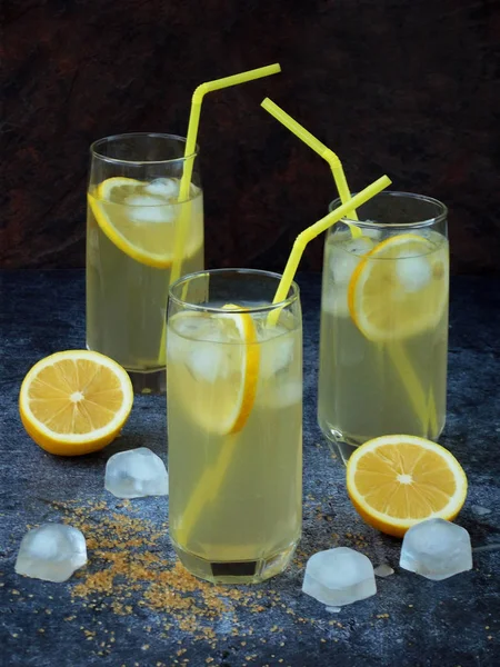 Drie glazen van koude zelfgemaakte limonade met citroen segmenten, ijsblokjes, bruine suiker en rietjes op donkere achtergrond. Kopiëren van ruimte — Stockfoto