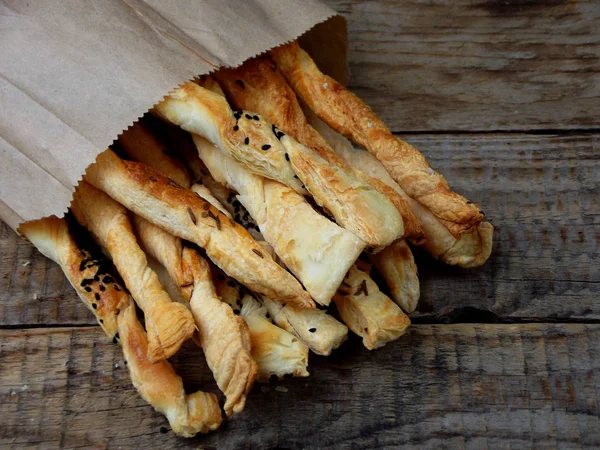 Salty sticks of puff pastry sprinkled with cumin and Nigella on a wooden background — Stock Photo, Image