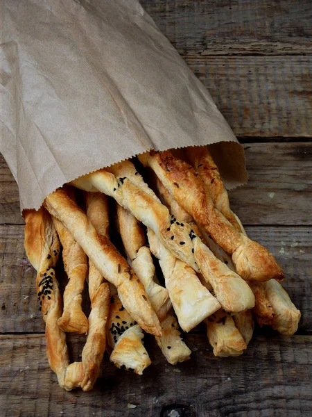 Slané tyčinky z listového těsta sypané kmínem a Nigella na dřevěné pozadí — Stock fotografie