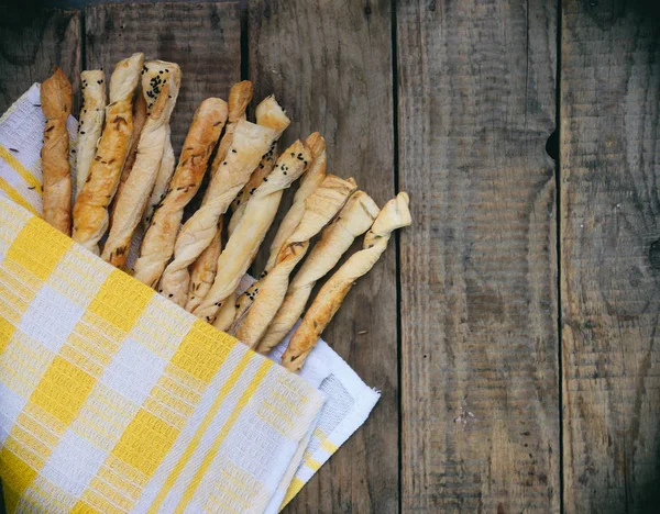 Salty sticks of puff pastry sprinkled with cumin and Nigella on a wooden background — Stock Photo, Image