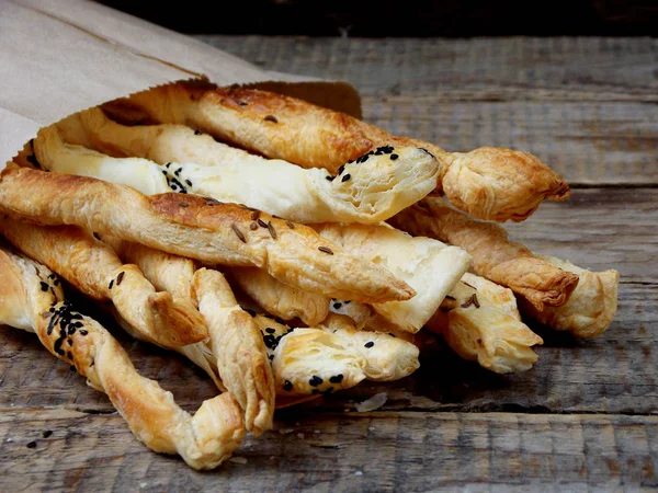 Salty sticks of puff pastry sprinkled with cumin and Nigella on a wooden background — Stock Photo, Image