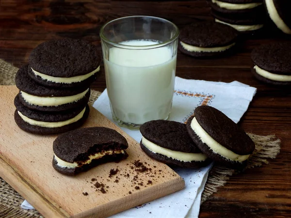 Biscoitos de chocolate caseiros com creme de marshmallow branco e vidro de leite no fundo escuro . — Fotografia de Stock