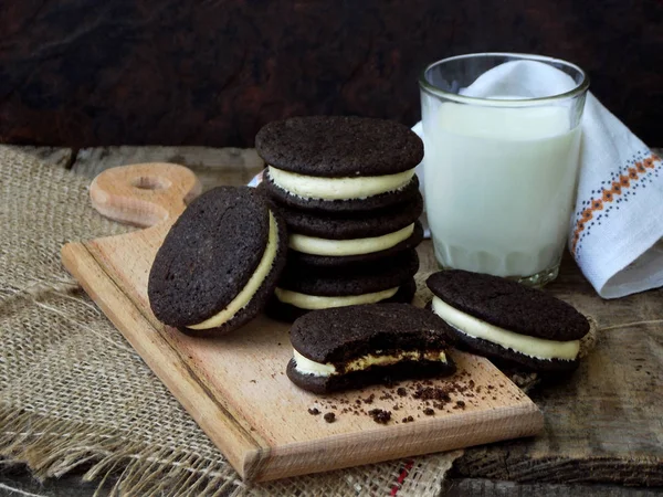 Hausgemachte Oreo-Schokoladenkekse mit weißer Marshmallow-Sahne und einem Glas Milch auf dunklem Hintergrund. — Stockfoto