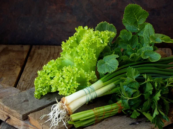 Verde primavera per insalata su uno sfondo di legno. Cipolla, lattuga, prezzemolo, foglie di ravanello . — Foto Stock