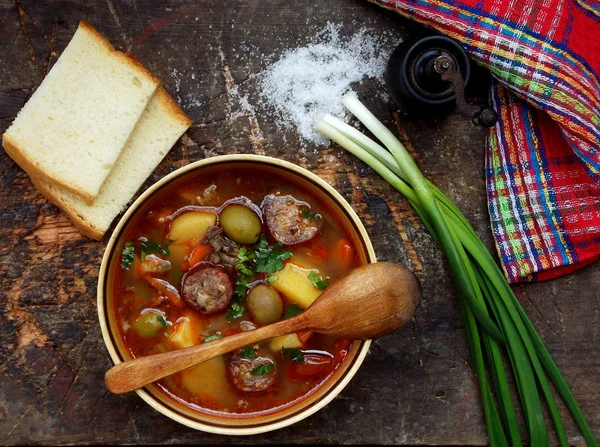 Kiadós házi leves burgonya, sárgarépa, kolbász és olajbogyó egy agyag edényben a fából készült háttér. — Stock Fotó