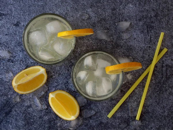 Glazen koude zelfgemaakte limonade met citroen segmenten, ijsblokjes en rietjes op donkere achtergrond. Kopiëren van ruimte — Stockfoto