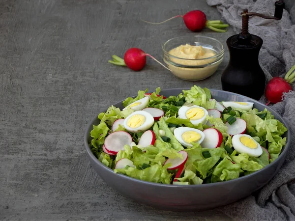 Insalata di vitamine da lattuga, ravanello, cipolle verdi e uova, condita con olio vegetale e senape in piatto su sfondo grigio cemento. Cibo sano. Spazio per testo — Foto Stock