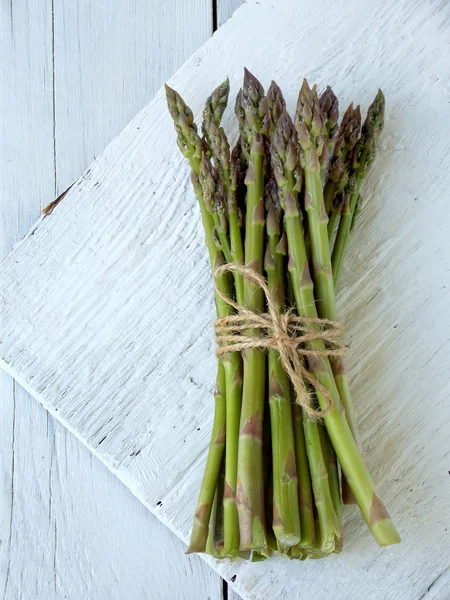 Bund frischer grüner Spargel auf hellem Holzgrund — Stockfoto