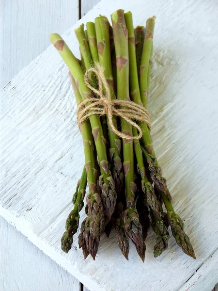 Bund frischer grüner Spargel auf hellem Holzgrund — Stockfoto