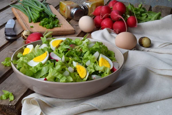 Vitaminsalat aus Salat, Rettich, grünen Zwiebeln und Eiern, gewürzt mit Pflanzenöl und Senf im Teller auf Holzboden. gesunde Ernährung. — Stockfoto