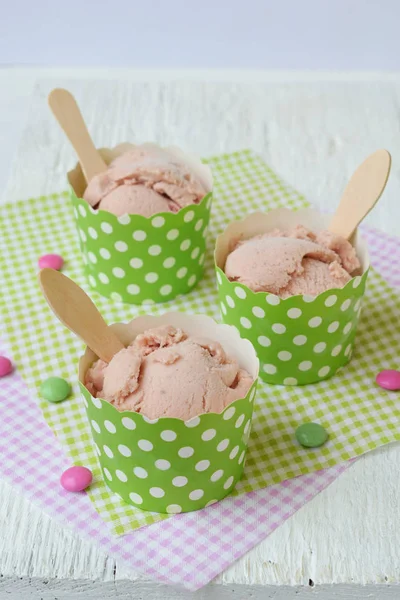 Pink milk ice cream in a paper cup on a white wooden background. Berry sorbet. Place for text