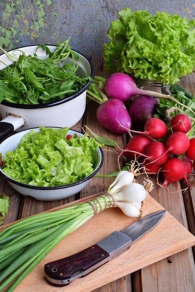 Verduras frescas de primavera: rábano, lechuga verde y púrpura, cebolla, rúcula sobre un fondo de madera. Preparación de alimentos, ensalada. Alimento saludable . — Foto de Stock