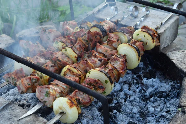 Barbecue marinated meat with onion and bacon. Shashlik or Shish kebab preparing on grill over charcoal in nature. Shashlyk skewered meat . BBQ grilling. — Stock Photo, Image