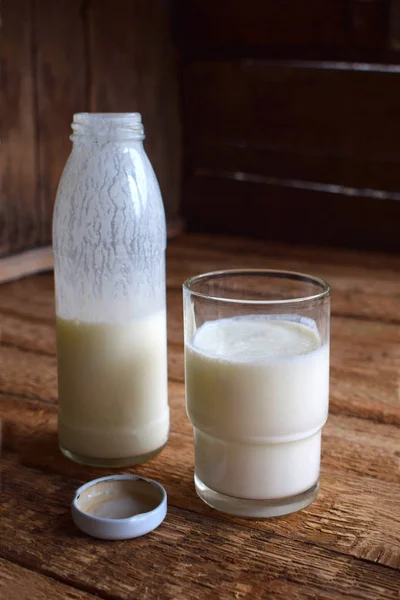 Bebida agria láctea o yogur en botella que proviene de los granos de kéfir y leche sobre fondo de madera. Fotografiado con luz natural — Foto de Stock