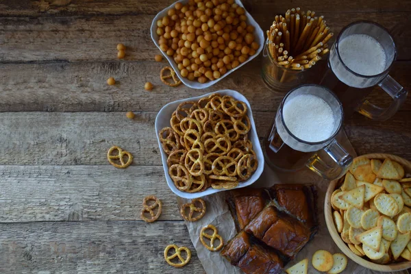 Football fan set with mugs of beer and salty snacks on wooden background. Crackers, pretzel, salted straws, nuts, dried fish. Junk food for beer or cola. Photographed with natural light — Stock Photo, Image