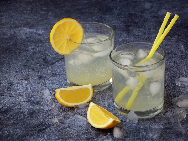 Glazen koude zelfgemaakte limonade met citroen segmenten, ijsblokjes en rietjes op donkere achtergrond. Kopiëren van ruimte. — Stockfoto