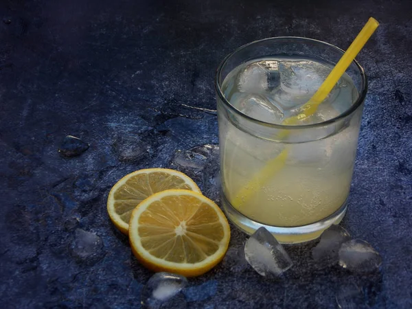 Glazen koude zelfgemaakte limonade met citroen segmenten, ijsblokjes en rietjes op donkere achtergrond. Kopiëren van ruimte. — Stockfoto