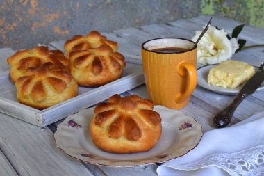 Ayran akşam yemeği buns çiçek formunda ahşap zemin üzerine tereyağı, bıçak ve fincan kahve ile devam eder. Taze pişmiş tatlı çörek. Homemade pişirme.
