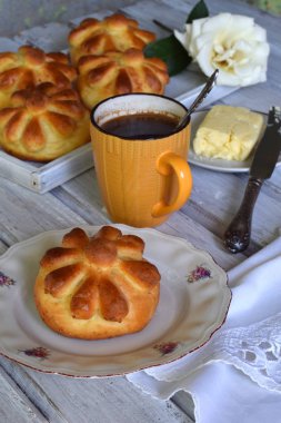 Ayran akşam yemeği buns çiçek formunda ahşap zemin üzerine tereyağı, bıçak ve fincan kahve ile devam eder. Taze pişmiş tatlı çörek. Homemade pişirme.
