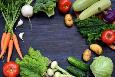 Vejetaryen Organik ürünlerin karanlık bir arka plan üzerinde kompozisyon: yeşil yapraklı sebzeler, havuç, kabak, patates, soğan, sarımsak, domates. Üstten Görünüm. Düz yatıyordu.