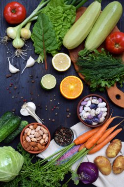 Vejetaryen Organik ürünlerin karanlık bir arka plan üzerinde kompozisyon: yeşil yapraklı sebzeler, narenciye, fındık, fasulye, havuç, kabak, patates, soğan, sarımsak, domates. Üstten Görünüm. Düz yatıyordu.