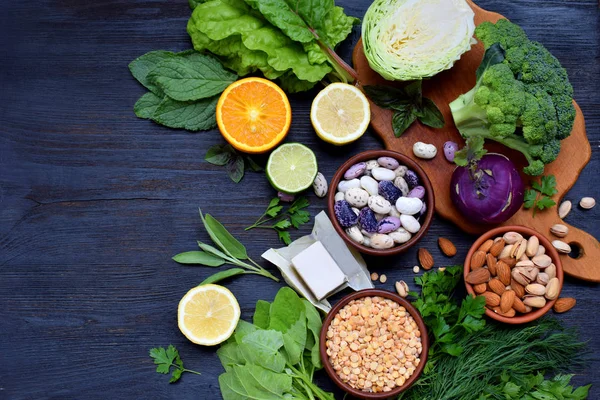 Composición sobre un fondo oscuro de productos que contienen ácido fólico, vitamina B9 - verduras de hoja verde, cítricos, frijoles, guisantes, nueces, levadura. Vista superior. Puesta plana — Foto de Stock