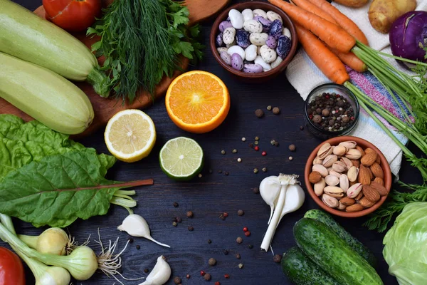 Composición sobre un fondo oscuro de productos orgánicos vegetarianos: verduras de hoja verde, cítricos, frutos secos, frijoles, zanahorias, calabacines, patatas, cebollas, ajo, tomates. Vista superior. Puesta plana . — Foto de Stock