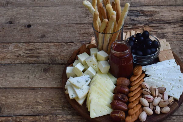 Assiettes de fromage servies avec grissini, craquelins, dattes, confiture, olives et noix sur fond de bois — Photo