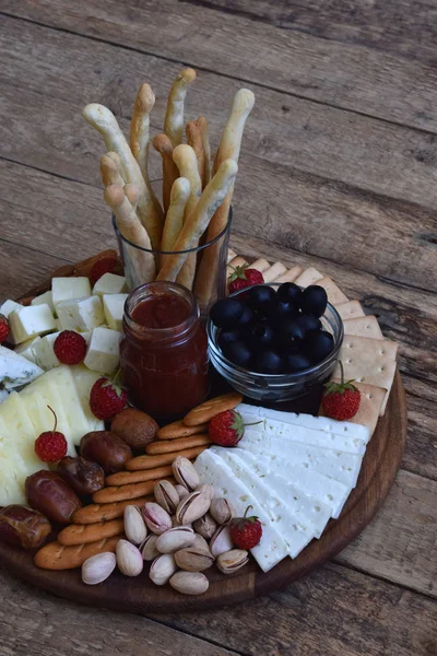 Pratos de queijo servidos com grissini, bolachas, tâmaras, compotas, azeitonas e nozes sobre fundo de madeira — Fotografia de Stock