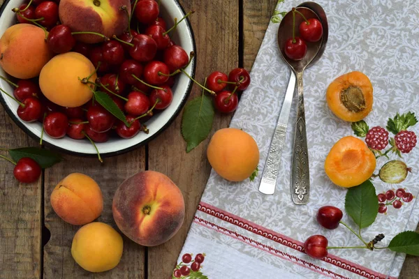 Свежие фрукты и ягоды на деревянном фоне. Спелые вишня и абрикос в миске на кухонном столе . — стоковое фото