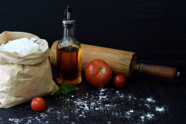Buğday unu, petrol, domates ve oklava çanta bileşimi. Hamur yoğurma, pasta ya da koyu arka plan üzerinde pizza pişirme için hazırlık. Metin için yer